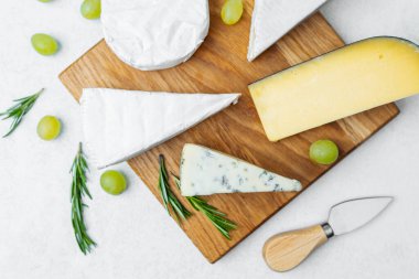 Tahta bir tahtanın üzerinde taze üzüm ve otlarla sergilenen çeşitli peynirler..