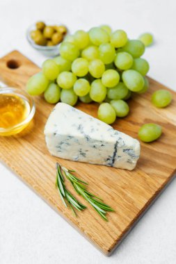 Tahtada taze yeşil üzüm, mavi peynir, bal ve bitkiler sergilenir..