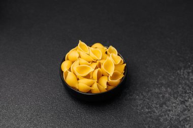 Taze sarı makarna kabukları, siyah bir kasede, karanlık bir yüzeyde düzgünce dizilmiş..