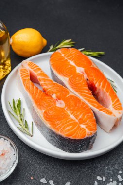 İki canlı somon filetosu limon ve otların yanında bir tabakta sergilenir..