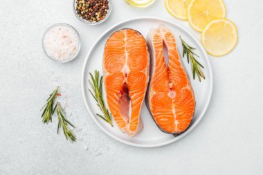 Somon filetoları bir tabakta otlar, limon dilimleri ve yakınlardaki baharatlarla sıralanmış..