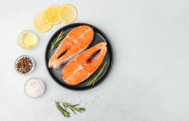 Somon filetoları bir tabakta otlar, yağ ve limon dilimleri pişirmeye hazırdır..