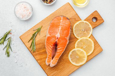 Taze somon, ahşap bir tahtanın üzerinde limon dilimleri ve otlarla sergilenir..