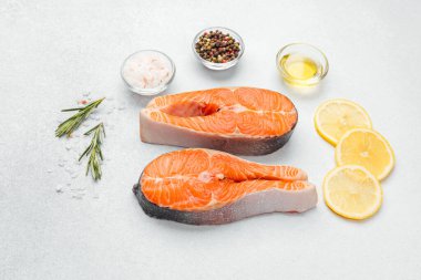 İki dilim somon fileto, limon dilimleri, otlar ve baharatlar düzgünce dizilmiş..