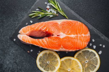 Parlak bir somon bifteği, limon dilimleri ve biberiyeyle dolu bir levha üzerine yerleştirilir..