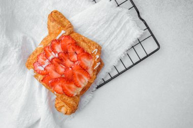 Üzerine taze dilimlenmiş çilek ve beyaz havluyla krema konmuş yumuşak hamur işi..