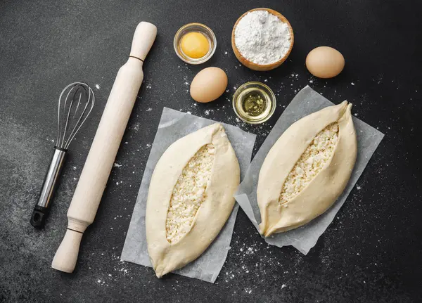 Malzemelerin üst görüntüsü ve iki pişmemiş khachapuri un kaplı siyah masa üzerinde