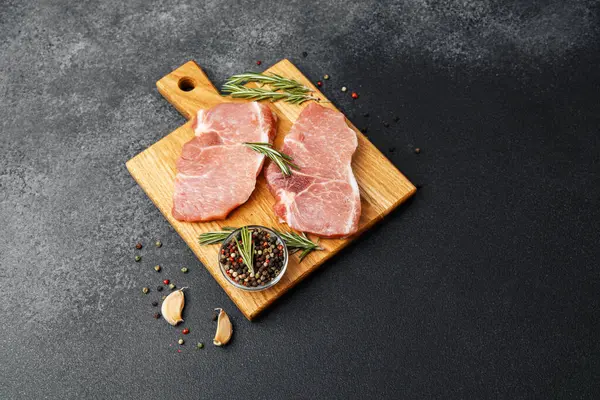 Ahşap bir tahtada iki çiğ domuz bifteği ve baharat..