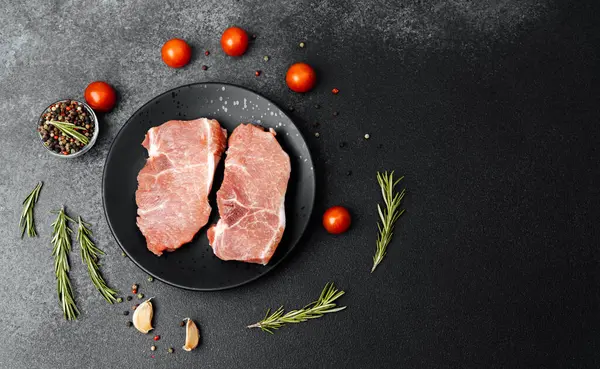 Siyah bir tabakta domuz pirzolası ve kiraz domatesleri pişmeye hazır..