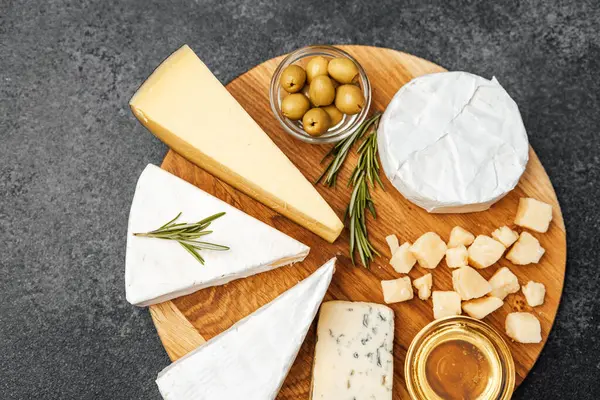 Tahta servis tahtasında zeytin ve bal ile sıralanmış çeşitli peynirler..