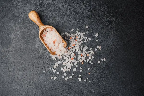 Koyu arkaplanda pembe himalaya tuzu olan ahşap kepçe.