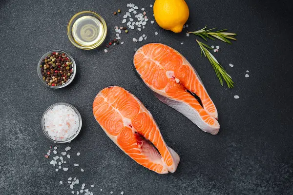 Somon filetoları, yakınlarda bitkiler ve baharatlarla birlikte koyu bir tezgahta hazırlanır..