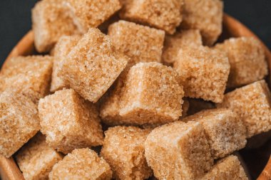 Kahverengi şeker küpleri, arka plandaki ahşap bir kasede düzgünce düzenlenir..