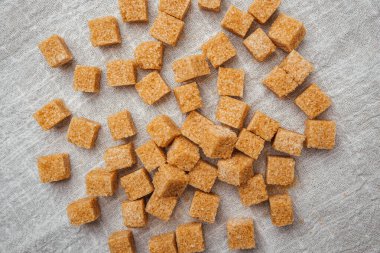 Kahverengi şeker küpleri açık renkli bir kumaşa yayılarak desenli bir görüntü oluşturur..