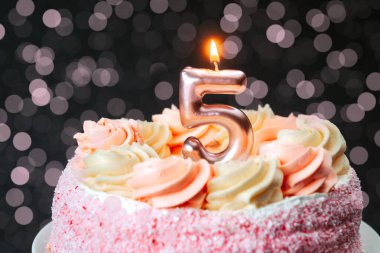 Pembe şekerle süslenmiş bir doğum günü pastası ve beş numaralı mum alevi..