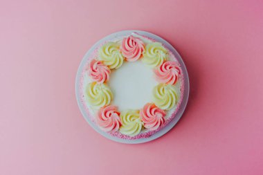 Pembe ve sarı kremalı parlak pasta. Pembe bir arkaplanda kıvrılıyor..