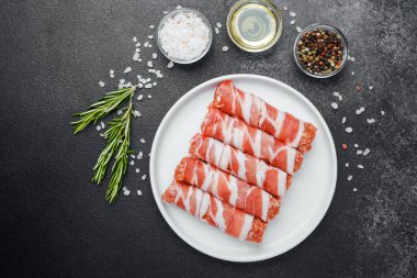 Çiğ domuz pastırması beyaz tabağa sarılmış, baharatlı ve otlu.