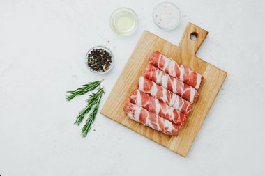 Domuz pastırmasına sarılı sosisli börekler, ahşap tahtada otlarla.