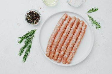 Biberiye ve baharatlı, beyaz tabakta pişmemiş sosisler.