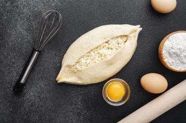 Süzme peynirli çiğ khachapuri ve siyah arka plandaki malzemeler.