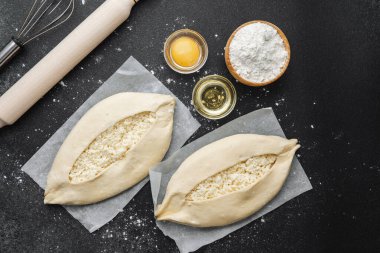 Malzemelerin üst görüntüsü ve iki pişmemiş khachapuri un kaplı siyah masa üzerinde