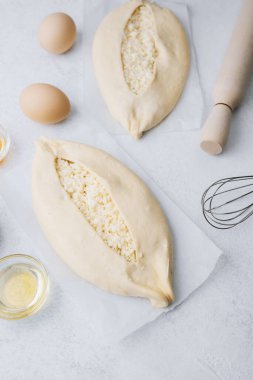 Işık yüzeyinde peynirli ve yumurtalı iki çiğ khachapuri.