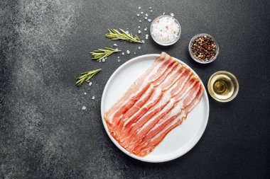 Beyaz tabakta çiğ domuz pastırması, biber, tuz ve biberiye.