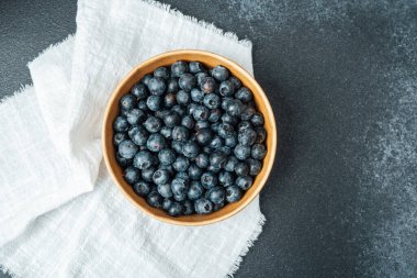 Yaban mersinleri yuvarlak ahşap bir kase içinde dokulu bir kumaş üzerinde düzgünce dizilir..