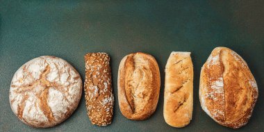 Koyu bir arkaplanda düzgün sıralanmış farklı zanaat ekmeklerinden oluşan bir seçim.