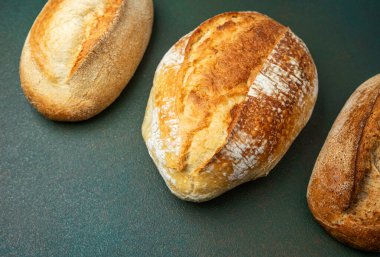 Üç çeşit kabuklu ekmek somunları karanlık bir yüzeyde sergilenir..