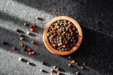 Çeşitli biberlerle dolu ahşap bir kase gölgeli karanlık bir yüzeyde oturur..