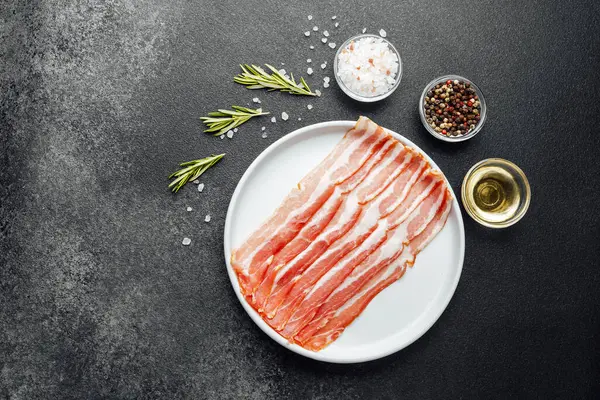 Beyaz tabakta çiğ domuz pastırması, biber, tuz ve biberiye.