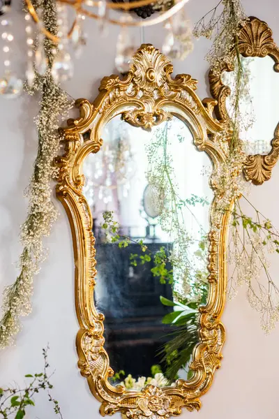 Altın çerçeveli güzel bir ayna yumuşak ışığı ve çiçekli süslemeleri yansıtır..