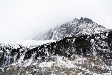 Karlı Chamonix dağ zirveleri sisli ve ormanlı kayalık yamaçlarla