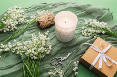 Çiçekli yanan mum ve yeşil kumaşlı hediye kutusu.