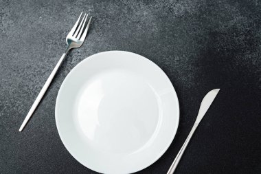 Temiz, basit bir tablo görüntüsünde yiyecek bekleyen boş bir tabak ve çatal bıçak bulunur..