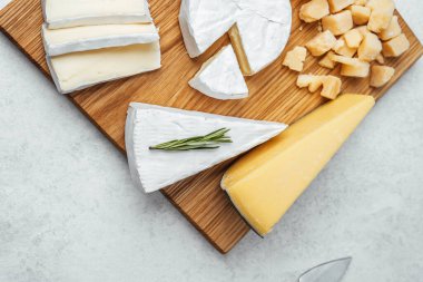 Tahta bir tahtanın üzerinde otlarla sergilenen taze kesilmiş peynir çeşitleri..