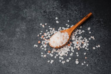 Ahşap kaşık pembe himalaya tuzu ve dokulu siyah yüzey.