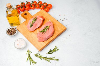 Domates, yağ, tuz ve biberiye ile çevrili ahşap kesim tahtasıyla çiğ dana bifteği.