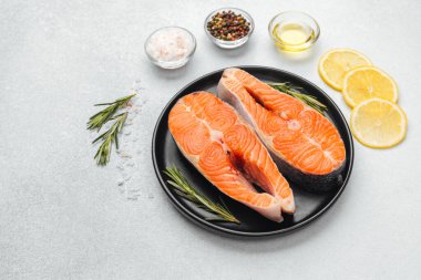 Somon filetoları, yanında taze otlar ve limon dilimleri olan koyu bir tabakta otururlar..