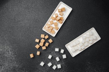 İki tip küp şeker, beyaz tepsiler üzerinde siyah bir zemin üzerinde düzgün bir şekilde düzenlenir..