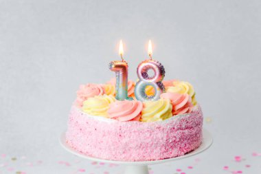 Renkli şekerlerle süslenmiş pembe bir doğum günü pastası ve 18 yaşını kutlayan mumlar..