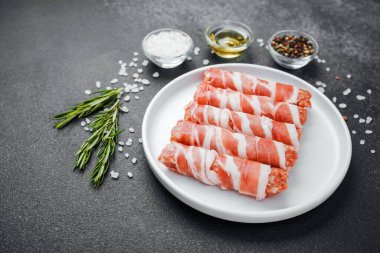 Çiğ domuz pastırması beyaz tabağa sarılmış, baharatlı ve otlu.