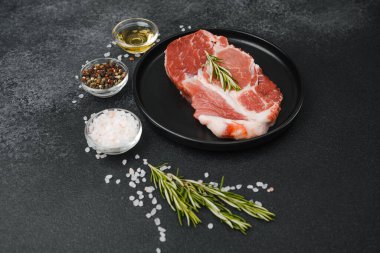 Çiğ biftek, otlar ve siyah tabakta baharatlar.