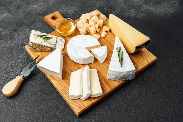 Bal ve otlarla ahşap bir kesim tahtasına dizilmiş bir peynir koleksiyonu..