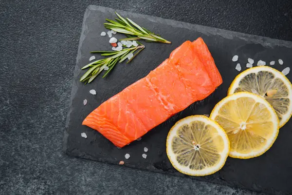 Canlı bir somon filetosu tahtanın üzerine konmuş limon dilimleri ve bitkilerle birlikte..
