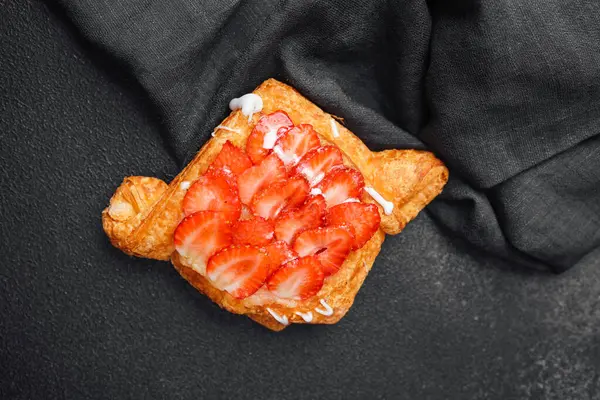 Dilimlenmiş çilek ve kremayla kaplı taze pişmiş hamur işi..