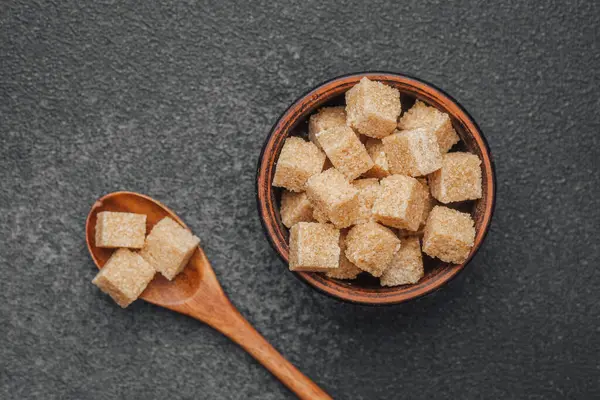 Kahverengi şeker küpleri özenle koyu arkaplandaki ahşap bir kasede düzenlenir..