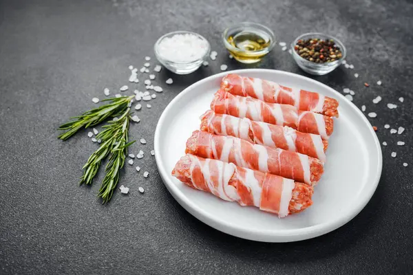 Çiğ domuz pastırması beyaz tabağa sarılmış, baharatlı ve otlu.