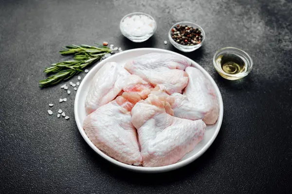 Baharatlı baharatlı tavuk kanatları ve koyu taşlı arka planda yağ.